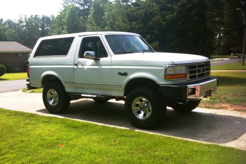 White 1993 Ford Bronco parked on a driveway with grass and trees in the background