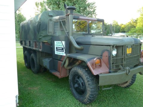 1992 Ford Mustang - This military cargo truck has camouflage paint and a tarped bed, with company text on its side.