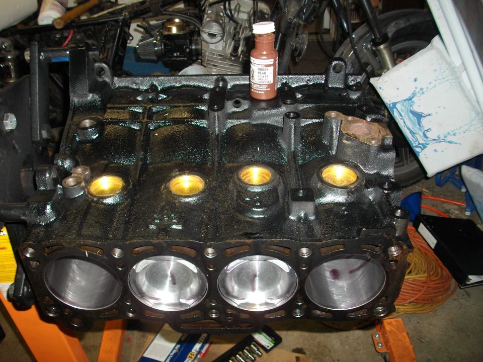 engine block with four cylinders and pistons visible, a bottle of fluid on top