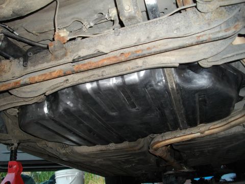 1989 Ford Probe - Underside view of a car's fuel tank and exhaust system, showing suspension components and rusted frame rails.