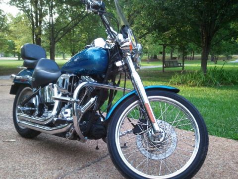 1967 Ford Mustang - A blue motorcycle with chrome accents is parked outdoors on a paved surface with a grassy area and trees in the background.
