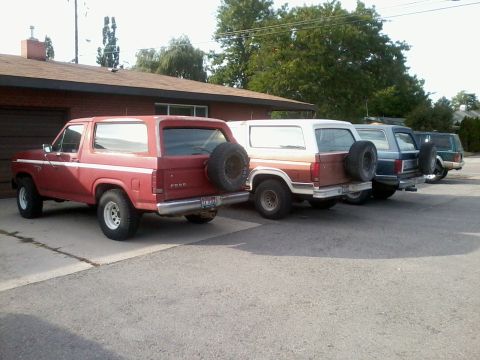 1981 Ford Bronco - A row of SUVs, including a red 1981 Ford Bronco, are parked in front of a building.