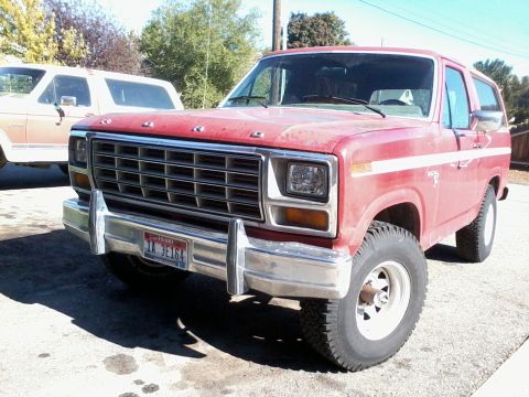1981 Ford Bronco - This red Ford Bronco is parked outside on a sunny day next to another Bronco.