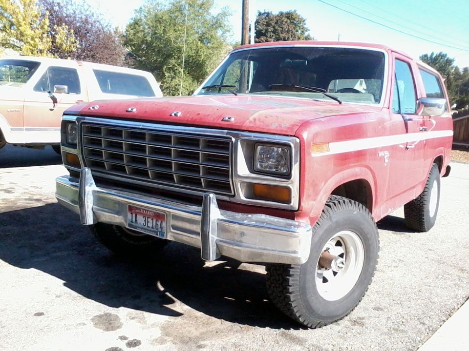 Red Ford Bronco parked next to a tan Ford Bronco. Front view
