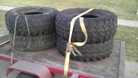 1989 Ford Bronco - Four off-road tires are strapped to a trailer, ready for transport.