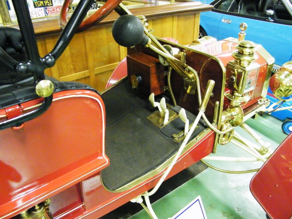 Red antique automobile interior with black floor mat, brass accents, and a large black steering wheel