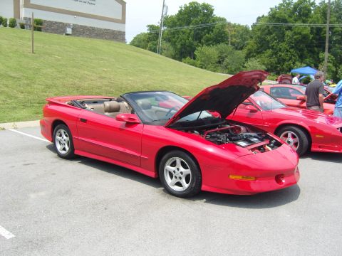 2007 Ford Mustang - A red convertible sports car is parked at an outdoor event, with its hood open, revealing the engine compartment.