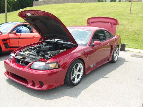 2007 Ford Mustang - A red Mustang is parked with its hood and trunk open, showing the engine and rear spoiler. Another Mustang is visible behind it.
