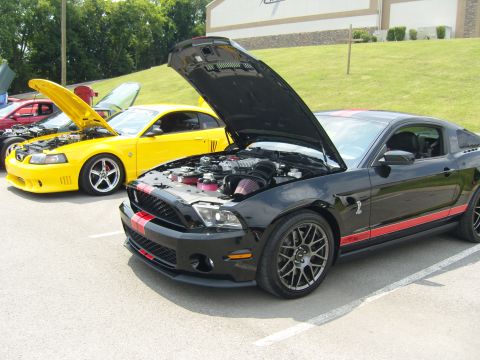 2007 Ford Mustang - A black 2007 Ford Mustang with red racing stripes is parked with its hood open, revealing the engine, alongside other cars at a show.