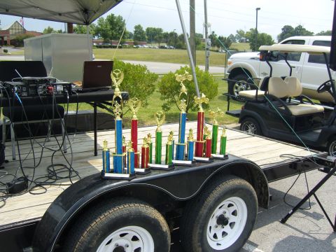 2007 Ford Mustang - A collection of trophies sits on a trailer, with a sound system and golf carts visible in the background.