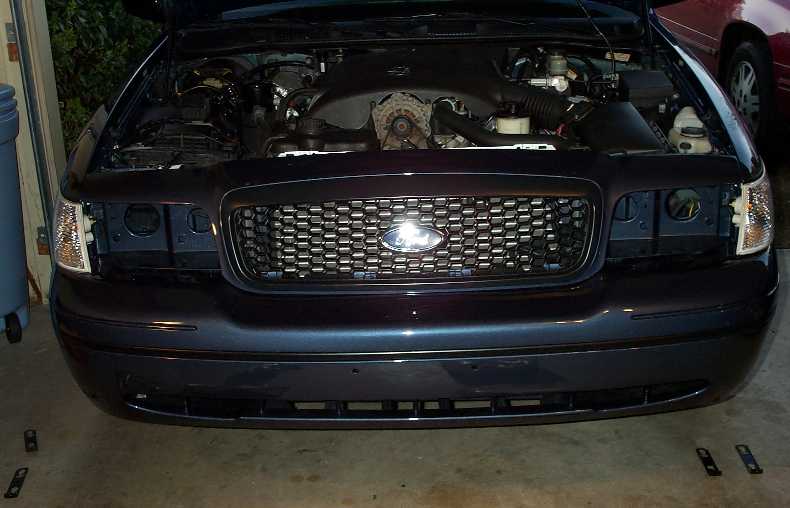 Open engine bay and front of dark Ford Crown Victoria in garage, mesh grille and front bumper off