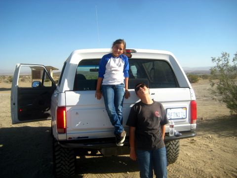 1996 Ford Bronco - Two children pose by a white 1996 Ford Bronco in a dry, open area under a clear blue sky.