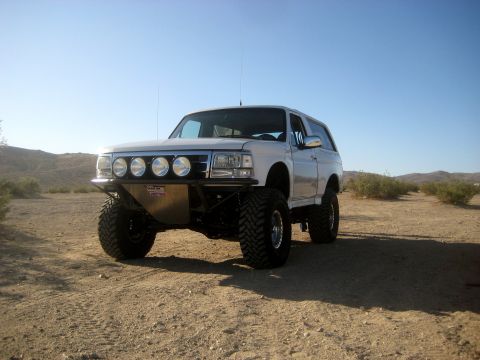 1996 Ford Bronco - A modified white Ford Bronco sits on a dusty, arid landscape under a clear blue sky.