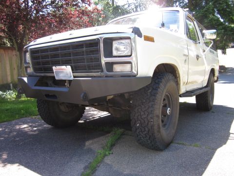 1989 Ford Bronco - This white Ford Bronco features an aftermarket bumper and off-road tires, seen from a 3/4 front angle.