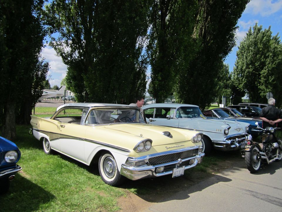 Yellow and white 1958 Ford Fairlane 500 parked next to other classic cars and a motorcycle