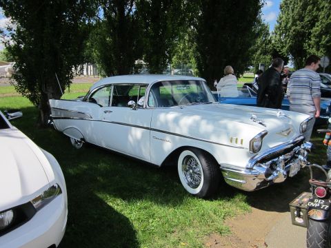 1991 Ford LTD Crown Victoria - A classic white 1957 Chevrolet Bel Air coupe is displayed outdoors, with other vehicles and people in the background.