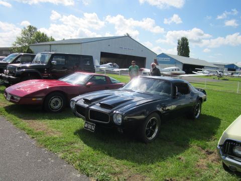 1991 Ford LTD Crown Victoria - A black Pontiac Firebird is parked on the grass in front of hangars with airplanes.