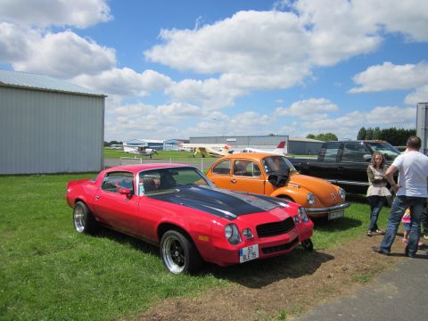 1991 Ford LTD Crown Victoria - A red 1977 Chevrolet Camaro is parked next to an orange VW Beetle and a black pickup truck at an outdoor event.