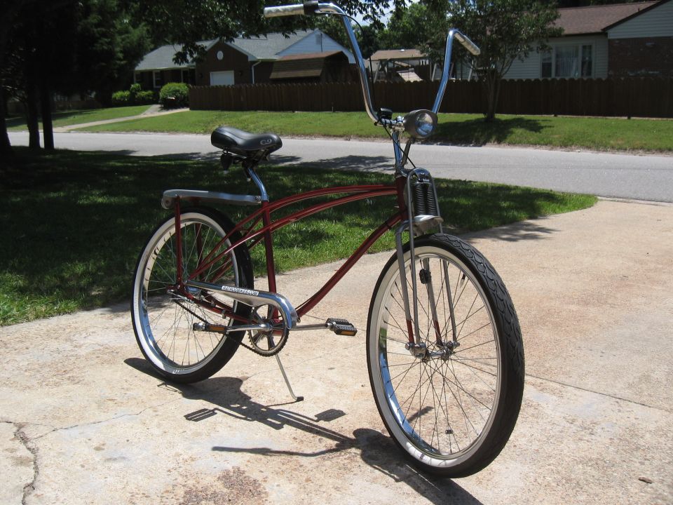 Red cruiser bicycle with chrome handlebars and whitewall tires parked on a concrete driveway
