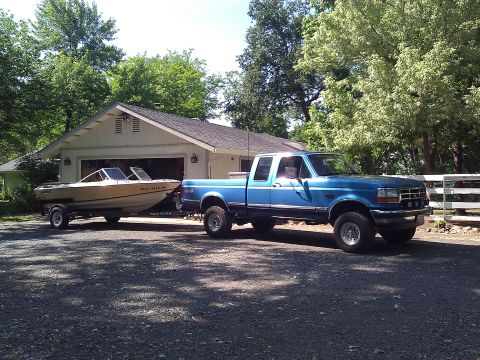 1992 Ford F-150 - A blue 1992 Ford F-150 pickup truck is parked in front of a garage, hitched to a boat on a trailer.
