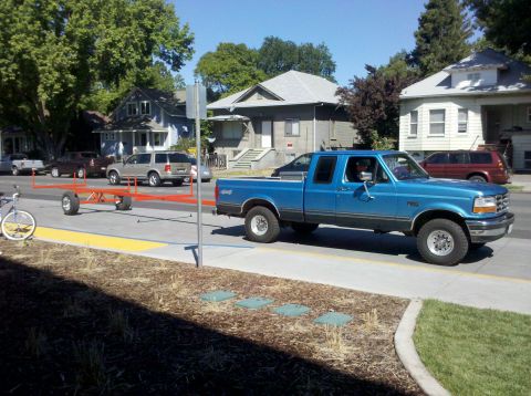 1992 Ford F-150 - A blue 1992 Ford F-150 pickup truck is seen driving down a street while towing a trailer.