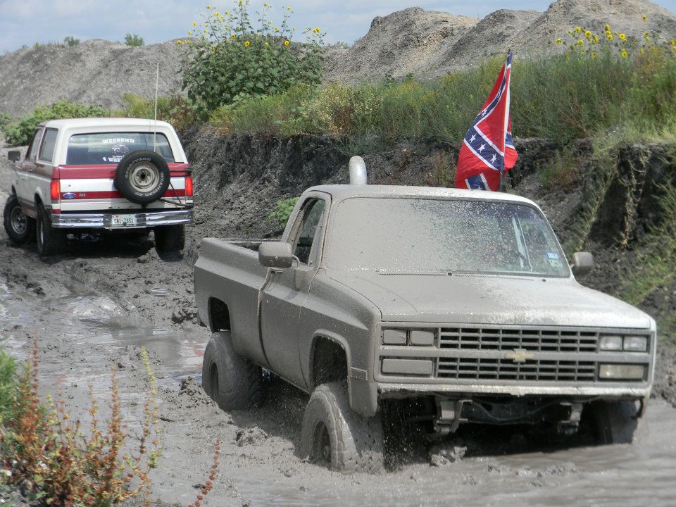 Muddy pickup truck stuck in mud with Bronco behind it. Confederate flag flying