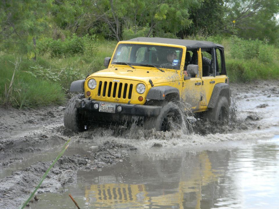 Yellow Jeep Wrangler driving through mud puddle, license plate reads CE1-1078