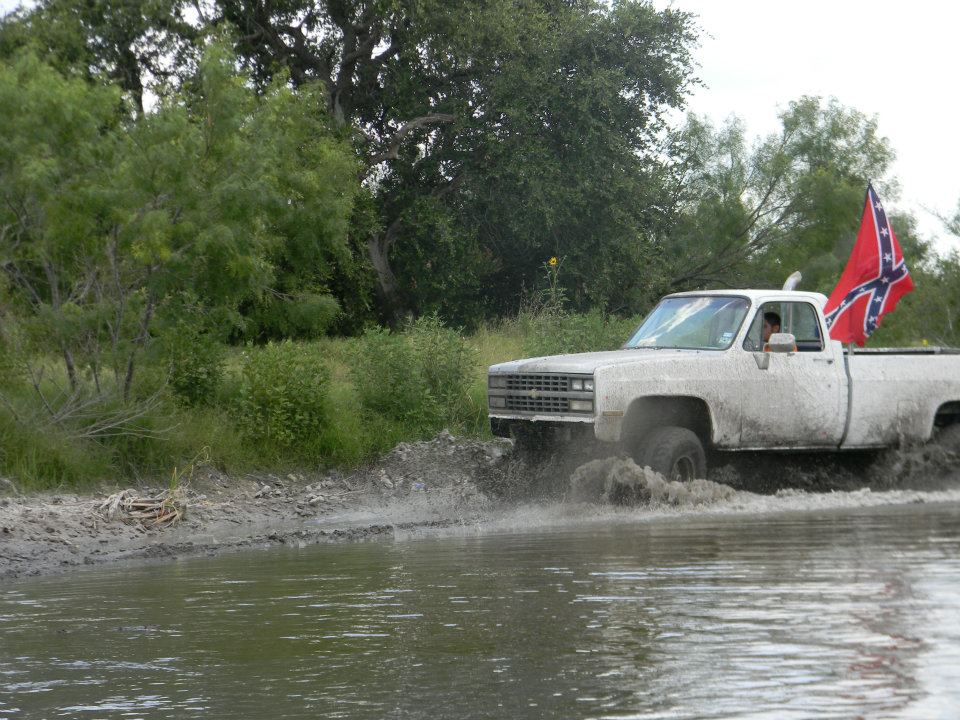 White pickup truck splashing through water, Confederate flag on back