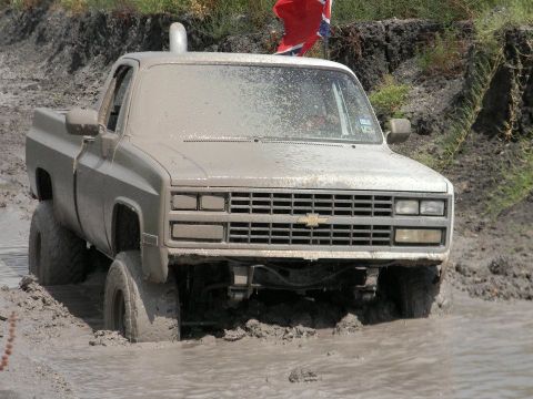1989 Ford Bronco - Pickup truck stuck deep in mud, with a Confederate flag visible in the background.