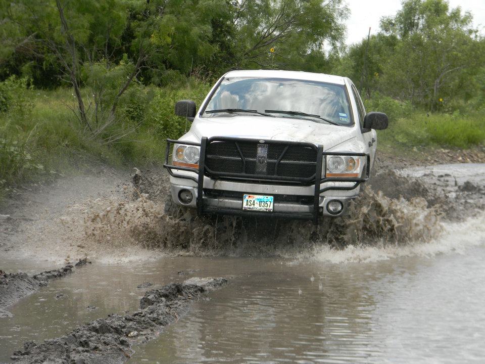 White pickup truck with a bull bar driving through a muddy puddle. License plate reads AS4-0357