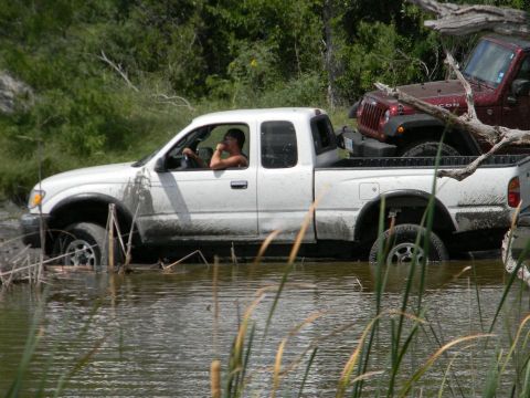 1989 Ford Bronco - Two off-road vehicles navigate through a muddy, watery terrain.