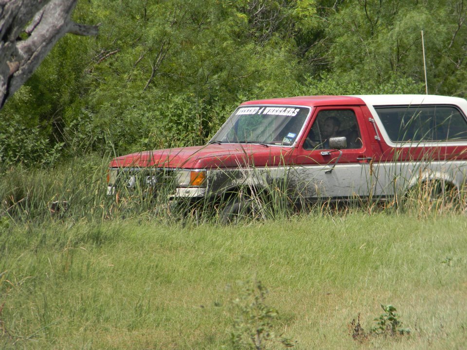 red and white SUV in tall grass, windshield banner reads 'TEXAS MUD & FREEDOM'