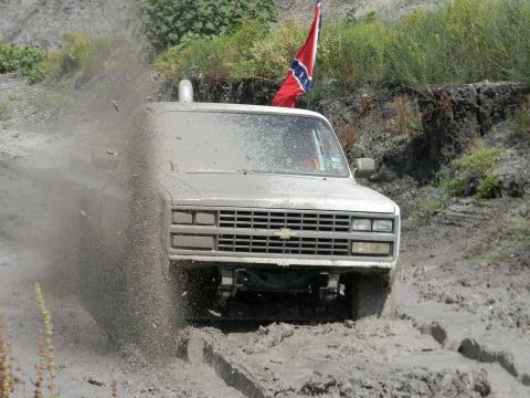 1989 Ford Bronco - A truck navigates a muddy terrain, kicking up dirt and water.