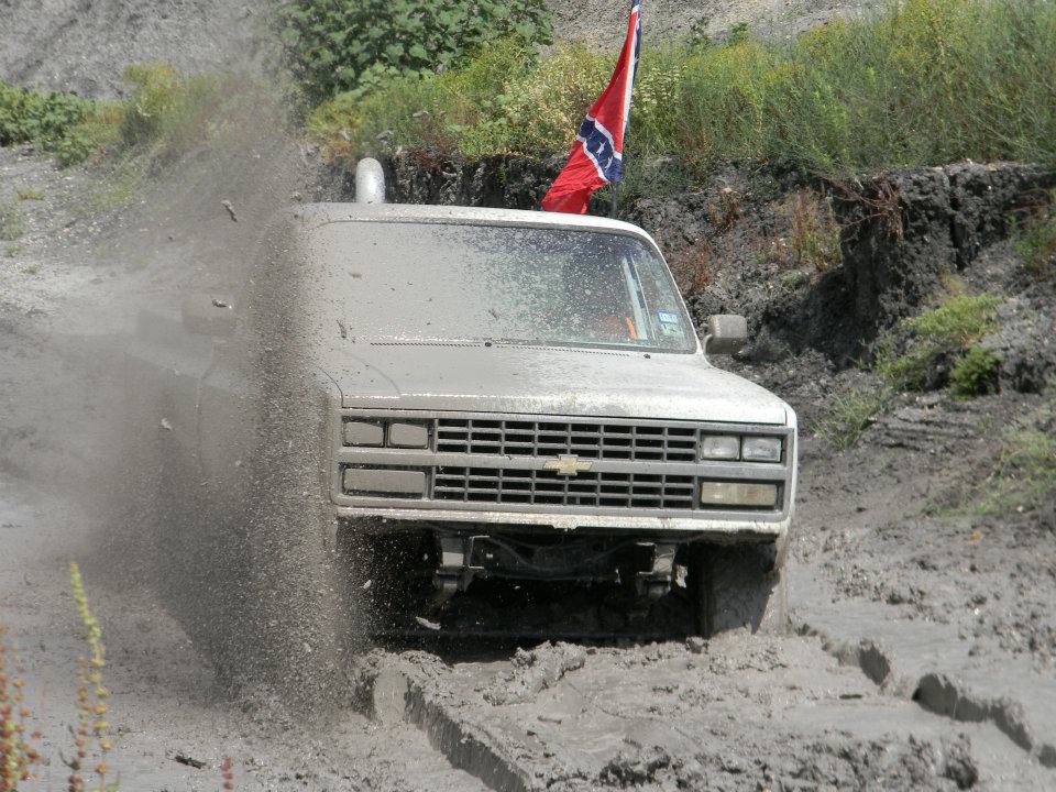 Mud-splattered truck with a Confederate flag driving through mud