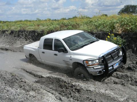 1989 Ford Bronco - A white pickup truck navigates a muddy terrain, with its front tires deep in the mire.