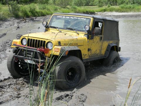 1989 Ford Bronco - This yellow Jeep Wrangler Rubicon is navigating through a muddy, watery terrain, kicking up spray.