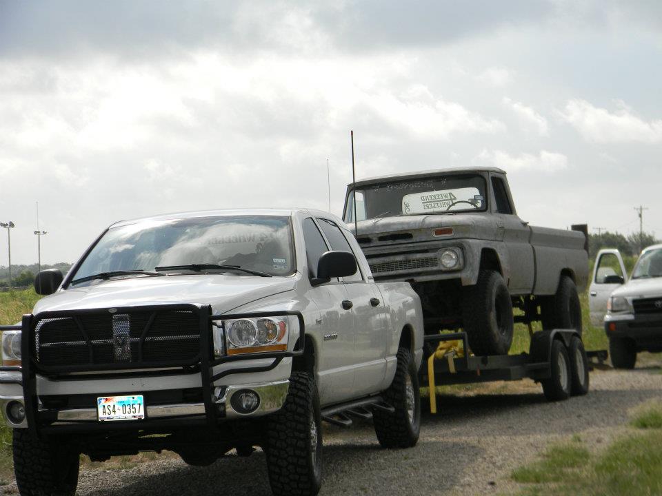 White pickup truck towing a grey pickup truck on a trailer