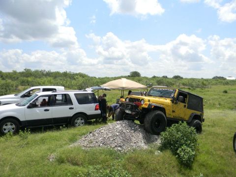 1989 Ford Bronco - Two off-road vehicles are gathered outdoors on a sunny day with a tent in the background.