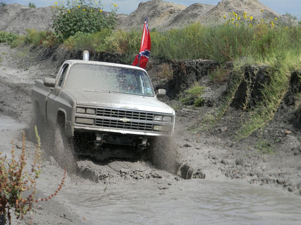 Pickup truck kicking up mud while driving off-road. It has a snorkel exhaust and a rebel flag on a pole