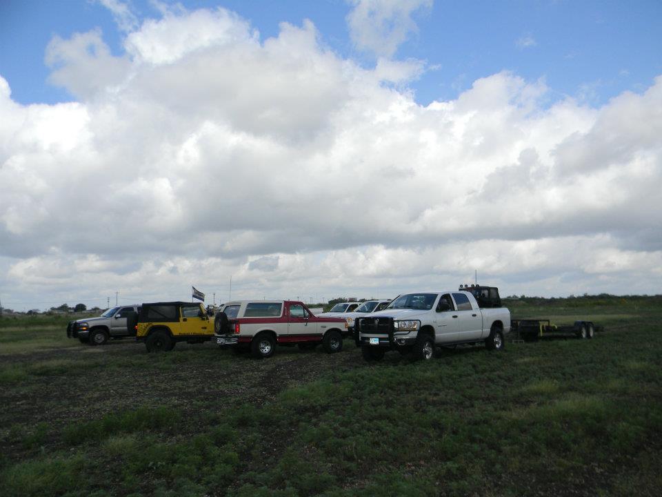 Red and white SUV parked in a grassy field with other vehicles and a trailer