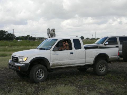 1989 Ford Bronco - A white Toyota pickup truck is seen from the side, with a driver giving the finger, parked next to another vehicle.