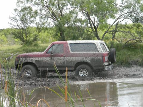 1989 Ford Bronco - This 1989 Ford Bronco is navigating a muddy off-road trail, kicking up water and mud.