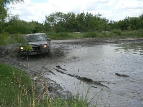1989 Ford Bronco - A GMC truck navigates a muddy terrain, kicking up water and mud.