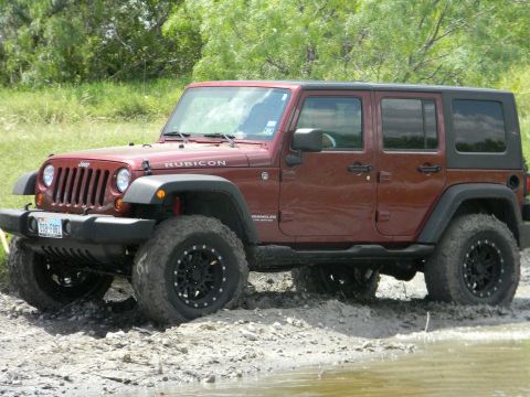 1989 Ford Bronco - This red Jeep Wrangler Rubicon navigates a muddy terrain, its off-road capabilities.