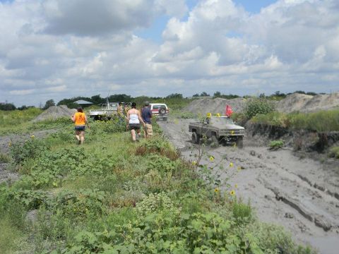 1989 Ford Bronco - Off-road vehicles navigate a muddy terrain with people observing the action.
