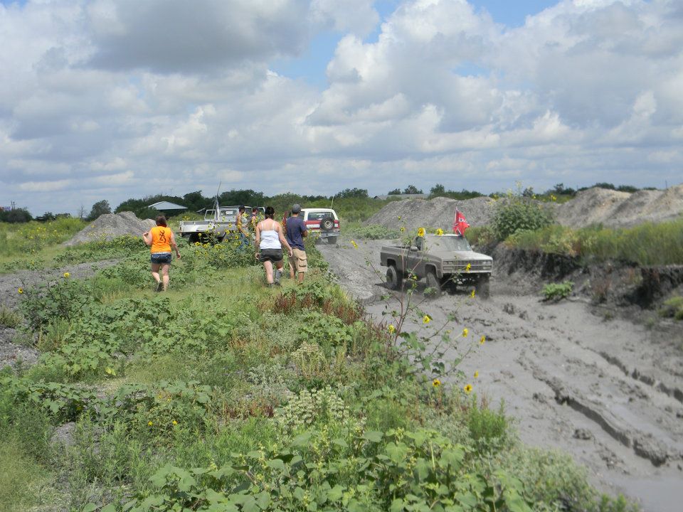 Several off-road vehicles driving through mud under a cloudy sky