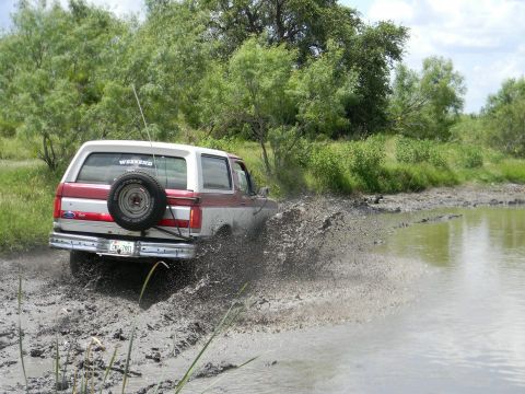 1989 Ford Bronco - This two-tone Ford Bronco is kicking up a lot of mud as it drives through a watery, muddy terrain.