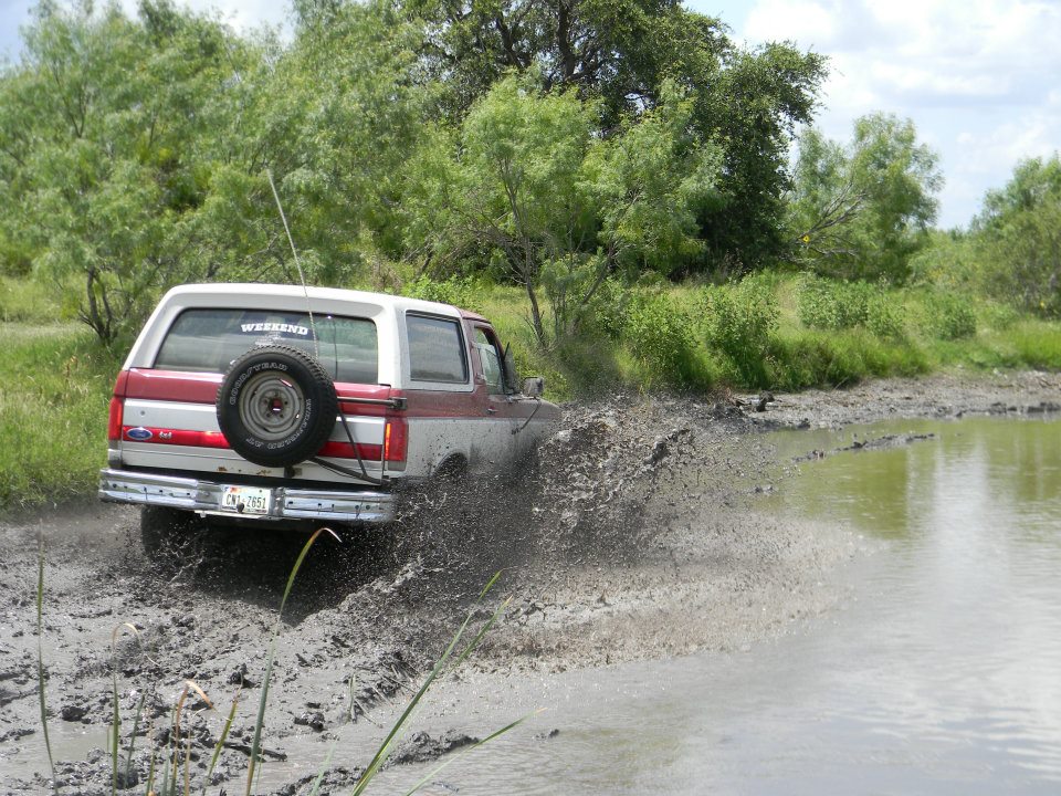 Ford Bronco driving through mud and water, spare tire on back. License plate reads CHT-7851