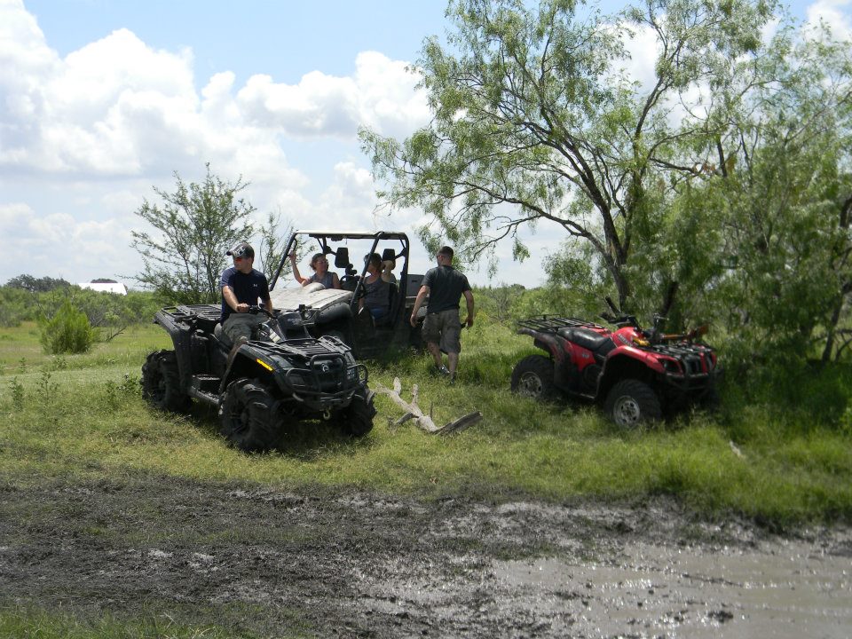 Black ATV in foreground, white side-by-side UTV with people in middle, red ATV in background, all in muddy terrain