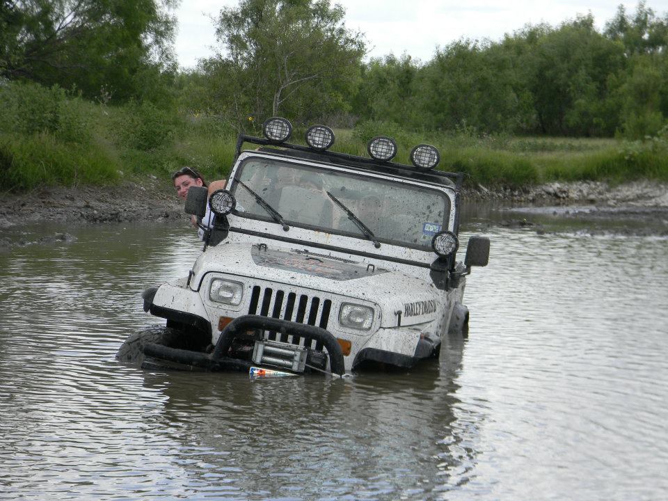 White Jeep Wrangler stuck in water, person in driver's seat looking out
